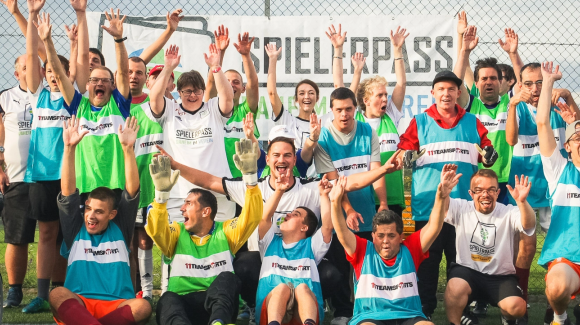 Jubelnde Sportler:innen mit und ohne Behinderung auf einem Sportplatz